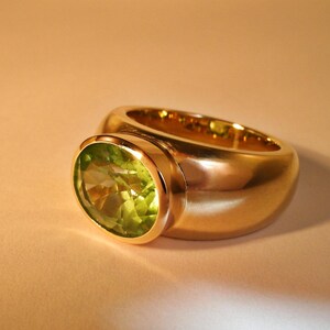 Seitenansicht des Goldrings, die die kraftvolle und massive Schiene aus 750er Gelbgold zeigt. Die Gestaltung ist minimalistisch und unterstreicht die Wertigkeit der Goldschmiedearbeit auf hellem Untergrund.