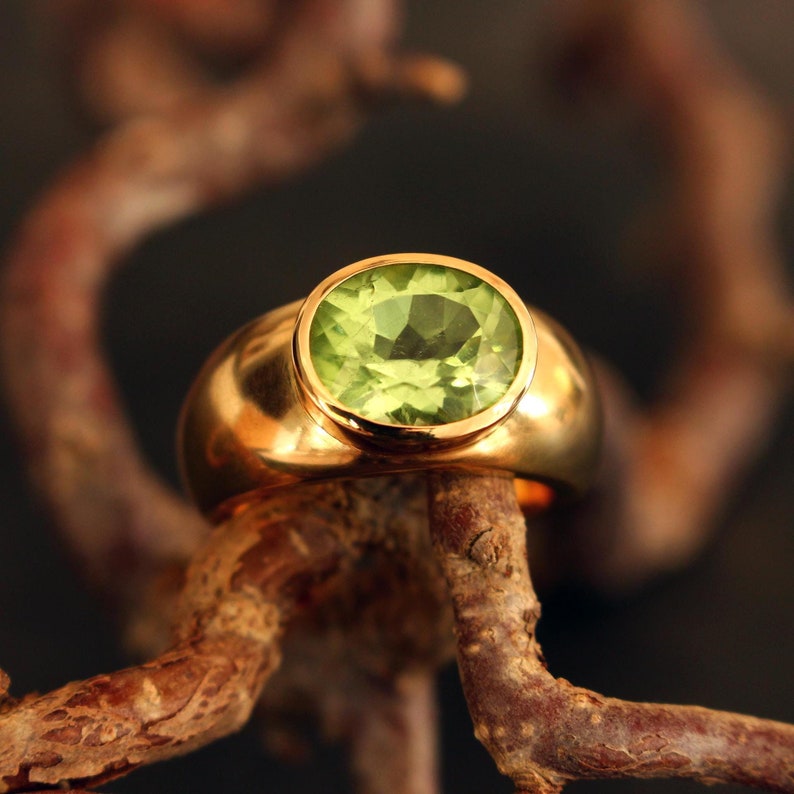 Handgeschmiedeter Solitärring aus massivem 750 Gelbgold (18 Karat) mit einem facettierten Peridot. Der Edelstein zeigt eine seltene, tiefe turmalingrüne Nuance und ruht auf einem natürlichen Zweig.