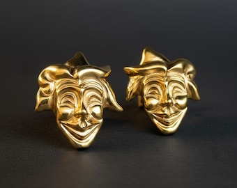 May include: A pair of polished gold-tone metal cufflinks, each featuring a three-dimensional sculpted jester face with a wide, smiling expression and a pointed cap. The metallic surface reflects light, highlighting the detailed facial features.