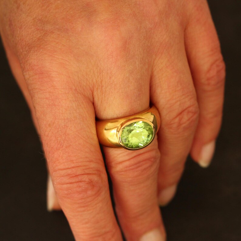 Ein massiver Peridot-Ring in 18 Karat Gelbgold, getragen an der Hand. Die Proportionen der breiten Goldschiene und die Wirkung der seltenen grünen Steinfarbe am Finger sind deutlich erkennbar.