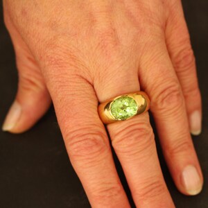 Ein massiver Peridot-Ring in 18 Karat Gelbgold, getragen an der Hand. Die Proportionen der breiten Goldschiene und die Wirkung der seltenen grünen Steinfarbe am Finger sind deutlich erkennbar.