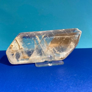 Peut inclure: Un cristal de quartz transparent avec une forme unique, présenté sur un support en acrylique transparent. Le cristal a une apparence naturelle légèrement nuageuse.
