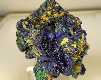 May include: A vibrant azurite mineral specimen with deep blue, green, and golden-yellow hues. The crystalline structure is visible, showcasing the natural beauty of the stone. The mineral is mounted on a clear stand.
