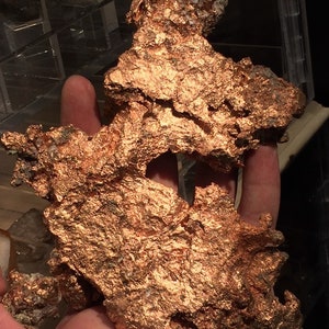 Puede incluir: Un gran trozo de mineral de cobre de forma irregular con una superficie rugosa y texturizada. El mineral es de color marr&oacute;n rojizo oscuro y tiene un brillo met&aacute;lico.
