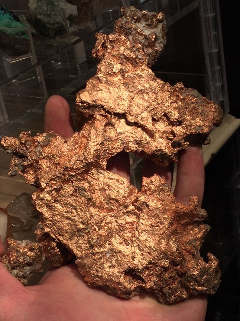 Puede incluir: Un gran trozo de mineral de cobre de forma irregular con una superficie rugosa y texturizada. El mineral es de color marr&oacute;n rojizo oscuro y tiene un brillo met&aacute;lico.