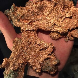 Puede incluir: Un gran trozo de mineral de cobre de forma irregular con una superficie rugosa y texturizada. El mineral es de color marr&oacute;n rojizo y tiene un brillo met&aacute;lico.