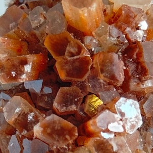 Puede incluir: Un cúmulo de cristales naranja y transparentes con un acabado brillante. Los cristales están dispuestos en un patrón aleatorio, creando una exhibición única e interesante.