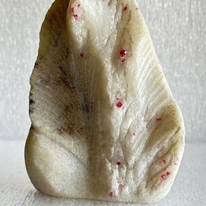 May include: A white, carved stone sculpture with a unique, organic shape. The stone is speckled with small, red crystals.
