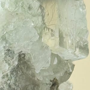 Puede incluir: Un grupo de cristales de fluorita transparentes, de color verde claro, con una base rugosa, gris y texturizada.