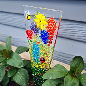 May include: A colourful glass garden stake featuring a bee, ladybug and flowers in shades of red, yellow, blue and green.