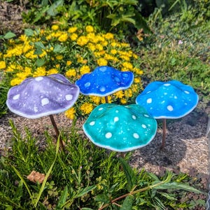 May include: Four ceramic mushroom garden decorations in a variety of colors, including purple, blue, and turquoise. Each mushroom has white polka dots.