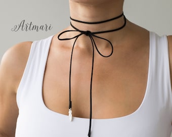 May include: Black choker necklace with a bow and dangling feather charms. The necklace is made of a thin, soft material and features two strands around the neck. The feather charms are silver-colored and add a delicate touch to the design.