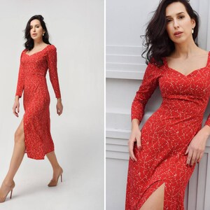 May include: A red midi dress with a white floral pattern and a side slit. The dress has a sweetheart neckline and long sleeves.