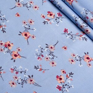 K&ouml;nnte beinhalten: Hellblauer Stoff mit einem sich wiederholenden Blumenmuster. Das Design zeigt kleine Gruppen von Bl&uuml;ten in Rosa, Pfirsich und Wei&szlig;, mit dunkelgr&uuml;nen Stielen und Bl&auml;ttern. Der Stoff ist gefaltet und zeigt seine Textur.