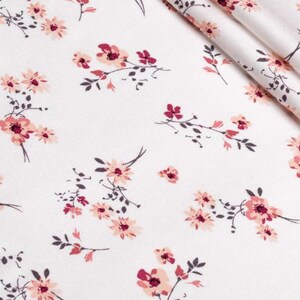 K&ouml;nnte beinhalten: Wei&szlig;er Stoff mit einem sich wiederholenden Blumenmuster. Das Design zeigt Gruppen von rosa und burgunderfarbenen Blumen mit dunkelgr&uuml;nen Stielen und Bl&auml;ttern. Der Stoff ist gefaltet und zeigt die Textur und das Muster.
