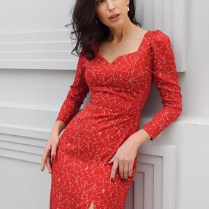 May include: A red midi dress with a white floral pattern and a thigh-high slit. The dress has a sweetheart neckline and long sleeves.