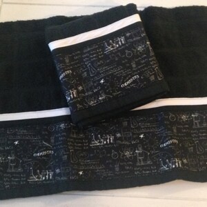 May include: Black bath towels with a white stripe and a decorative band featuring chemistry-themed illustrations and the word "CHEMISTRY". The towels are folded and stacked, showcasing the design.