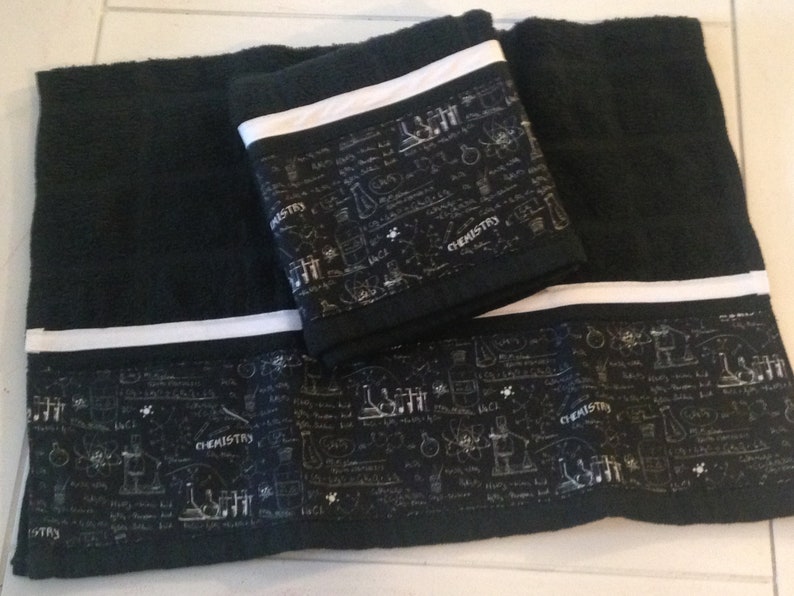 May include: Black bath towels with a white stripe and a decorative band featuring chemistry-themed illustrations and the word "CHEMISTRY". The towels are folded and stacked, showcasing the design.