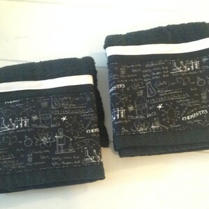 May include: Two black hand towels with a white stripe and a science-themed border. The border features chemistry-related illustrations and the word "CHEMISTRY" in white. The towels are folded.