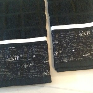 May include: Two black hand towels with a white stripe and a decorative band featuring chemistry-themed illustrations in white. The towels are made of a soft, absorbent material, perfect for the bathroom or kitchen.