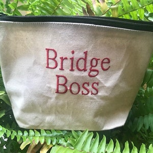 May include: A white canvas zippered pouch with a black zipper and red embroidered text that says "Bridge Boss".