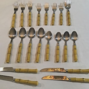 Puede incluir: Un juego de cubiertos vintage con mangos de bambú. La imagen muestra tenedores, cucharas y cuchillos con mangos de color amarillo claro y cabezas de acero inoxidable. La disposición sugiere un juego de comedor completo, adecuado para varias comidas.