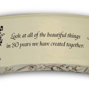 May include: A white ceramic garden stone with a curved shape and a floral design. The stone has the text "Look at all of the beautiful things in 30 years we have created together."
