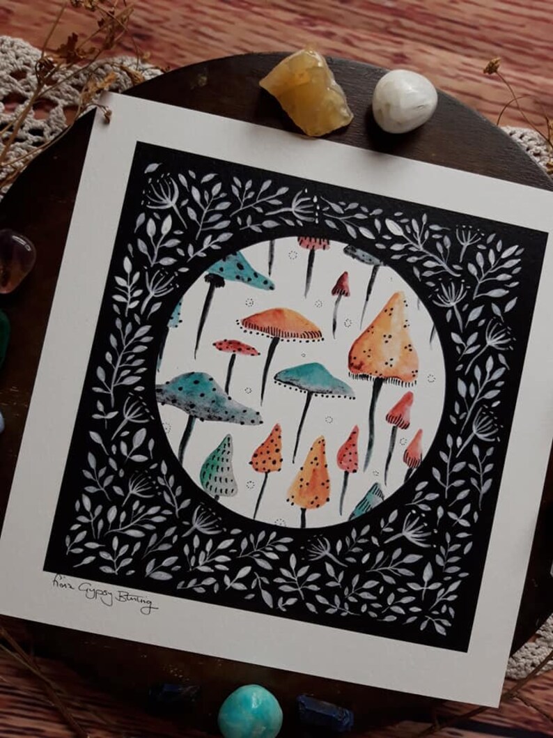 May include: A black and white illustration of a circle filled with colorful mushrooms. The circle is surrounded by a black border with white floral designs. The text "Nina Gypsy Burning" is in the bottom left corner.