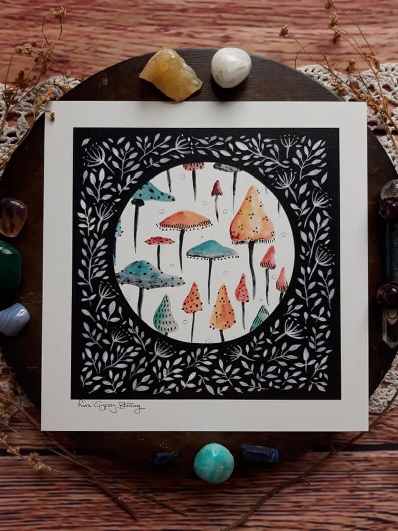 May include: A black and white illustration of a circle filled with colorful mushrooms. The mushrooms are various shades of orange, red, green, and blue. The circle is surrounded by a black frame with white leaves and branches.