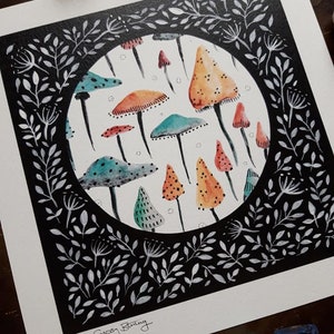 May include: A black and white illustration of a circle filled with colorful mushrooms. The circle is surrounded by a black frame with white leaves and branches. The artist's signature, "Ann Gypsy Bunting", is in the bottom left corner.
