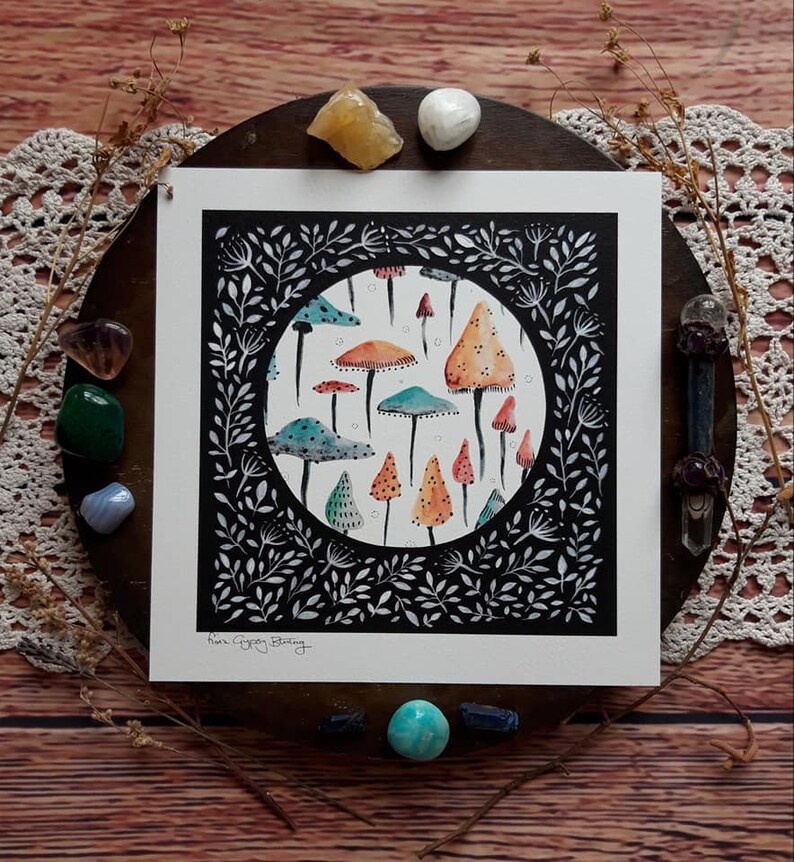 May include: A black and white illustration of a circle filled with colorful mushrooms. The mushrooms are various shades of orange, red, yellow, and blue. The circle is surrounded by a black border with white leaves and vines.