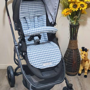 May include: A black stroller with a blue and white gingham patterned seat and canopy. The stroller has a black frame, wheels, and a storage basket. The seat has a safety harness. The brand name "FUNKY BABYZ" is visible on the seat.