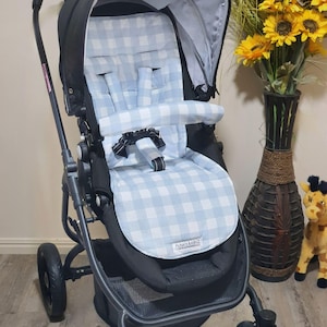 May include: A black stroller with a light blue and white gingham patterned seat and canopy. The stroller has a black frame and wheels. The seat has a five-point harness. The brand name "FUNKY & BABYZ" is visible on the seat.