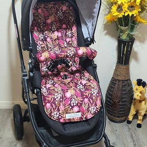 May include: A black stroller with a floral patterned seat in shades of burgundy, pink, and white. The stroller has a black frame, wheels, and a canopy. The text "FUNKY BABYZ" is visible on the seat.