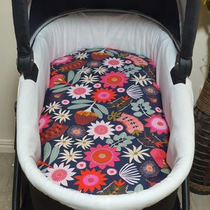 May include: A baby stroller with a navy blue floral patterned insert. The insert features pink, orange, and white flowers with green leaves. The stroller has a white interior and a black exterior.