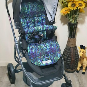 May include: A black stroller with a patterned seat in shades of blue, green, and purple. The stroller has a sunshade and a safety harness. The wheels are black, and the frame is dark gray. The stroller has the text "FUNKY BABYZ" on the seat.