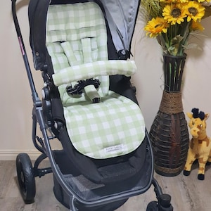 May include: A black stroller with a green and white checkered seat and canopy. The stroller has three wheels and a storage basket. The seat has a safety harness. The text "FUNKY BABYZ" is visible on the seat.