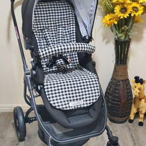 May include: A black and white gingham patterned stroller with a black frame. The stroller has a canopy, a seat with a safety harness, and a storage basket. The wheels are black. The stroller has the text "FUNKY BABY" on the front.