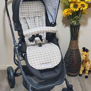 May include: A black stroller with a beige and white checkered pattern seat and canopy. The stroller has a black frame, wheels, and a storage basket. The text "FUNKY BABYZ" is visible on the seat.
