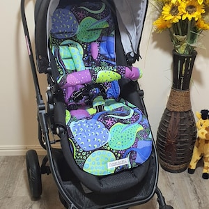 May include: A black stroller with a patterned seat featuring blue, green, and purple designs. The stroller has a black frame, wheels, and a canopy. The seat has the text "FUNKY BABYZ".