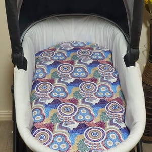 May include: A baby stroller with a white interior and a patterned insert. The insert features a colorful design with blue, purple, yellow, and red circular patterns. The stroller has a black frame and canopy.