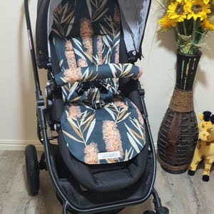 May include: A black stroller with a patterned seat featuring a dark teal background and orange and white floral design. The stroller has a black frame, canopy, and wheels. The stroller is designed for infants and toddlers.
