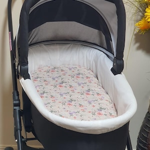 May include: A black and white baby stroller with a floral patterned interior. The stroller has a black frame, a white interior, and a canopy. The floral pattern includes pink, purple, and white flowers on a beige background.