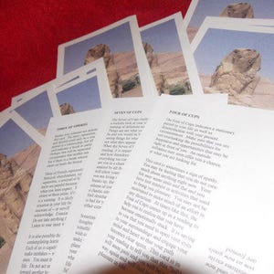 May include: A stack of white paper cards featuring a photographic print of the Great Sphinx of Giza in a desert landscape. Each card contains printed text describing tarot card meanings, specifically the Three of Swords, Seven of Cups, and Four of Cups.