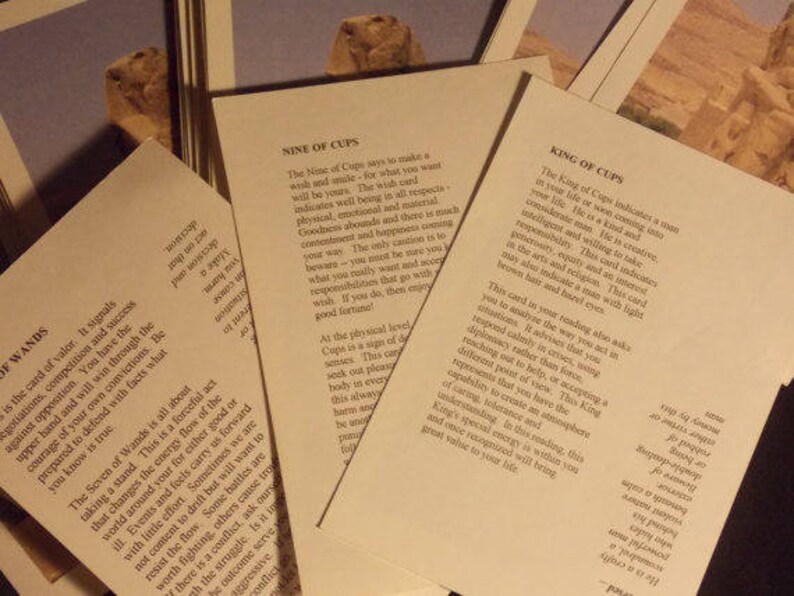 May include: Three off-white rectangular cards with black printed text describing tarot card meanings. The cards are titled Nine of Cups, King of Cups, and Seven of Wands. Each card features a small color image of a desert landscape at the top.