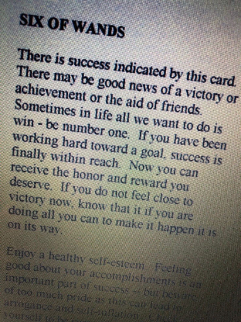 May include: A printed card or page titled SIX OF WANDS in bold black text. The text describes the card's meaning, stating there is success indicated, good news of a victory, achievement, or aid of friends. It mentions working hard toward a goal.
