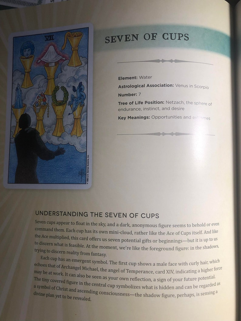 May include: A page from a book featuring the Seven of Cups tarot card illustration. The card shows a dark figure facing seven floating golden cups containing various symbols, including a face, a cloth, jewels, a wreath, and a dragon.
