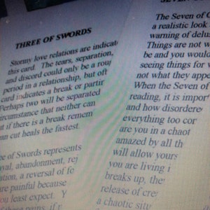 May include: A printed page featuring text about tarot cards, specifically the Three of Swords and the Seven of Cups. The text describes the Three of Swords as indicating stormy love relations, tears, and separation, while the Seven of Cups text discusses delusions and things not being what they appear to be.