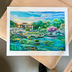May include: A colorful painting of a Japanese garden with a pagoda, a bridge, a pond with lily pads, and a pink flowering tree. The painting is done in a vibrant style with bold strokes and bright colors.
