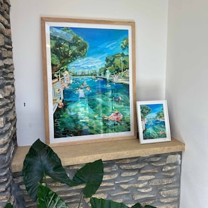 K&ouml;nnte beinhalten: Zwei gerahmte Kunstdrucke, die eine Schwimmbadszene mit schwimmenden und treibenden Personen zeigen. Der gr&ouml;&szlig;ere Druck ist in einem hellen Holzrahmen, der kleinere in einem wei&szlig;en Rahmen. Das Wasser ist klar t&uuml;rkis, mit gr&uuml;nen B&auml;umen und blauem Himmel.
